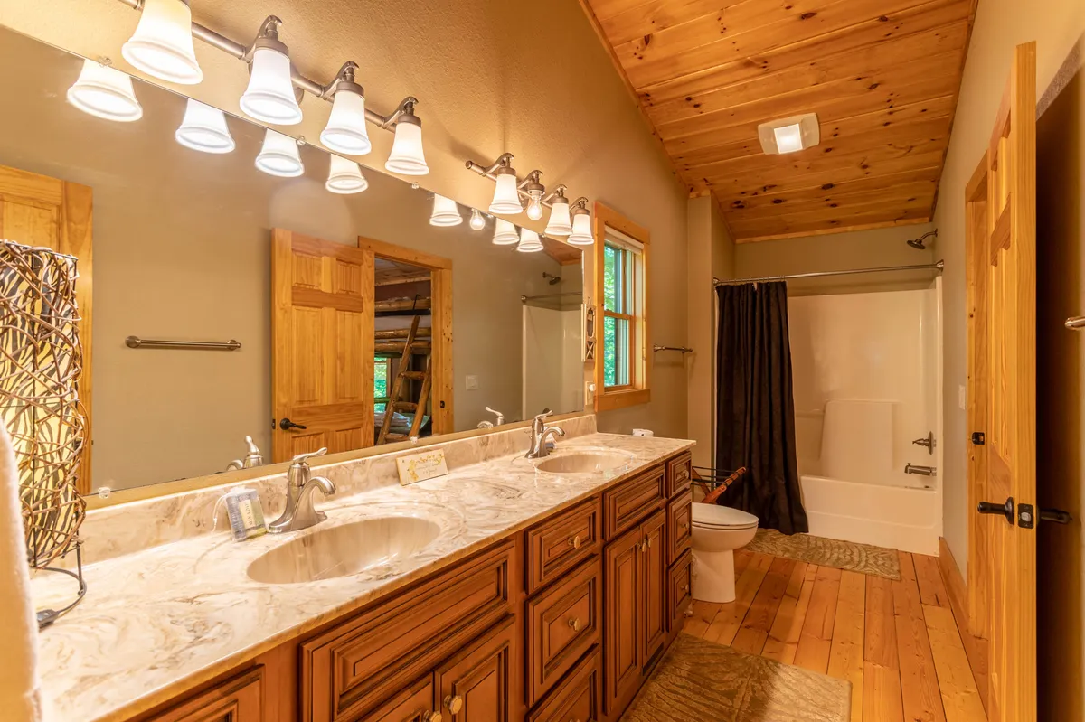 A spacious bathroom featuring a double sink vanity with marble countertops, wooden cabinetry, elegant light fixtures, and a shower area. The tranquil setting is perfect for morning routines or relaxing baths, with enough space for shared or individual use.