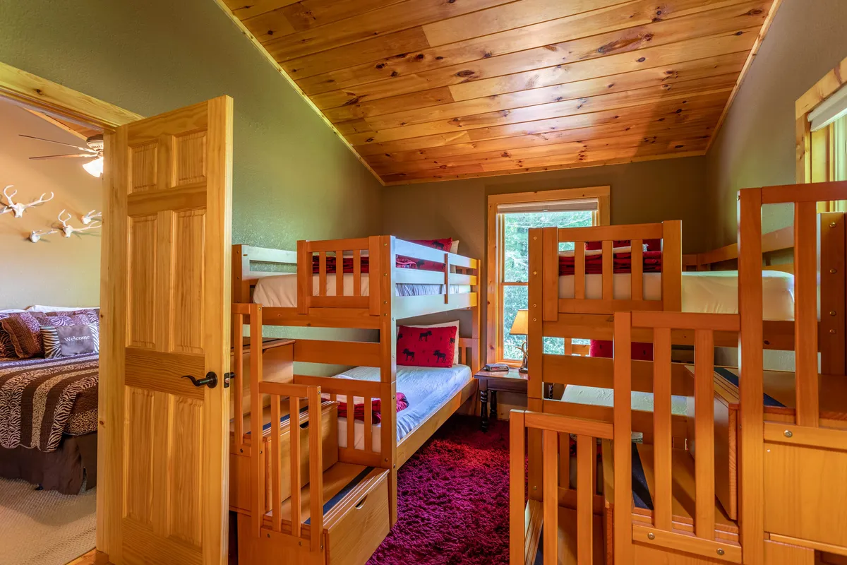 A cheerful bedroom with sturdy bunk beds, a window letting in natural light, a soft rug, and a small bedside table. The playful yet comfortable setup makes it ideal for kids to create lasting memories, read, or wind down after a day of adventures.