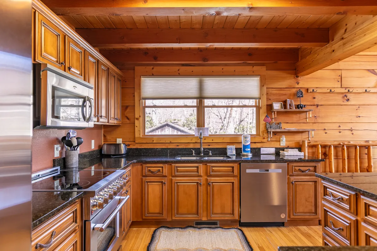 A bright kitchen scene featuring stainless steel appliances, wooden cabinetry, sleek granite countertops, and a large window overlooking scenic views. The atmosphere is both cozy and modern, perfect for a variety of group culinary activities.