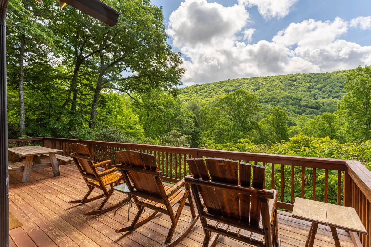 A spacious wooden deck with classic rocking chairs overlooking a lush green landscape. The deck offers panoramic views of the surrounding nature, making it an ideal spot to unwind after a bustling day of family activities in the area.