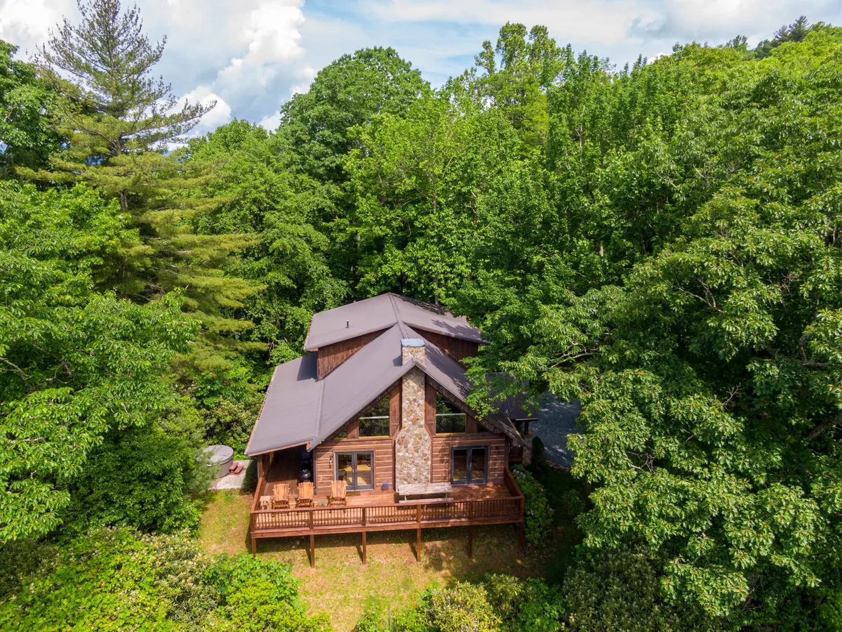 This exterior shot highlights the wooden deck of Azalea Hill, framed by large windows and a stone facade. The deck is surrounded by lush greenery, capturing the essence of the home's connection to nature. It’s an inviting space where guests can gather, relax, and enjoy the mountain views and changing seasons.