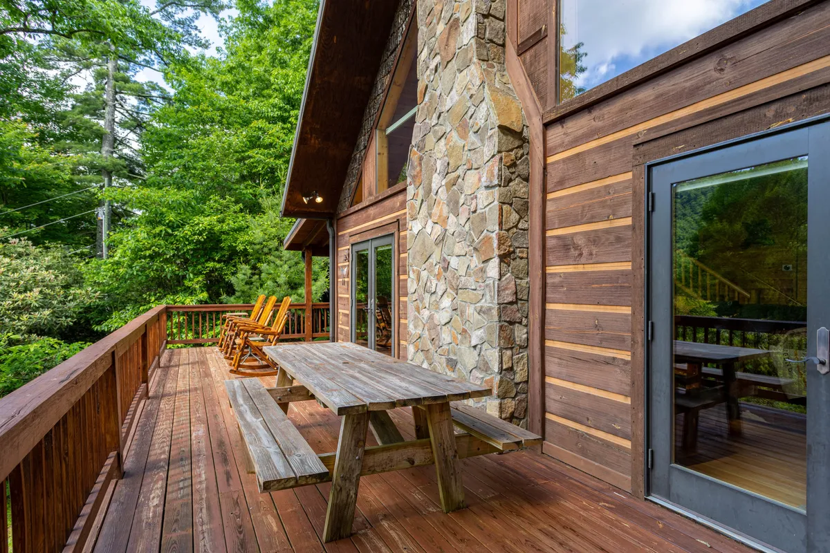 This image showcases a spacious wooden deck equipped with rocking chairs and a picnic table, all set against the backdrop of natural greenery. The stone wall and cozy seating arrangement make this a perfect spot for relaxing, dining, or simply enjoying the views that change with the seasons.