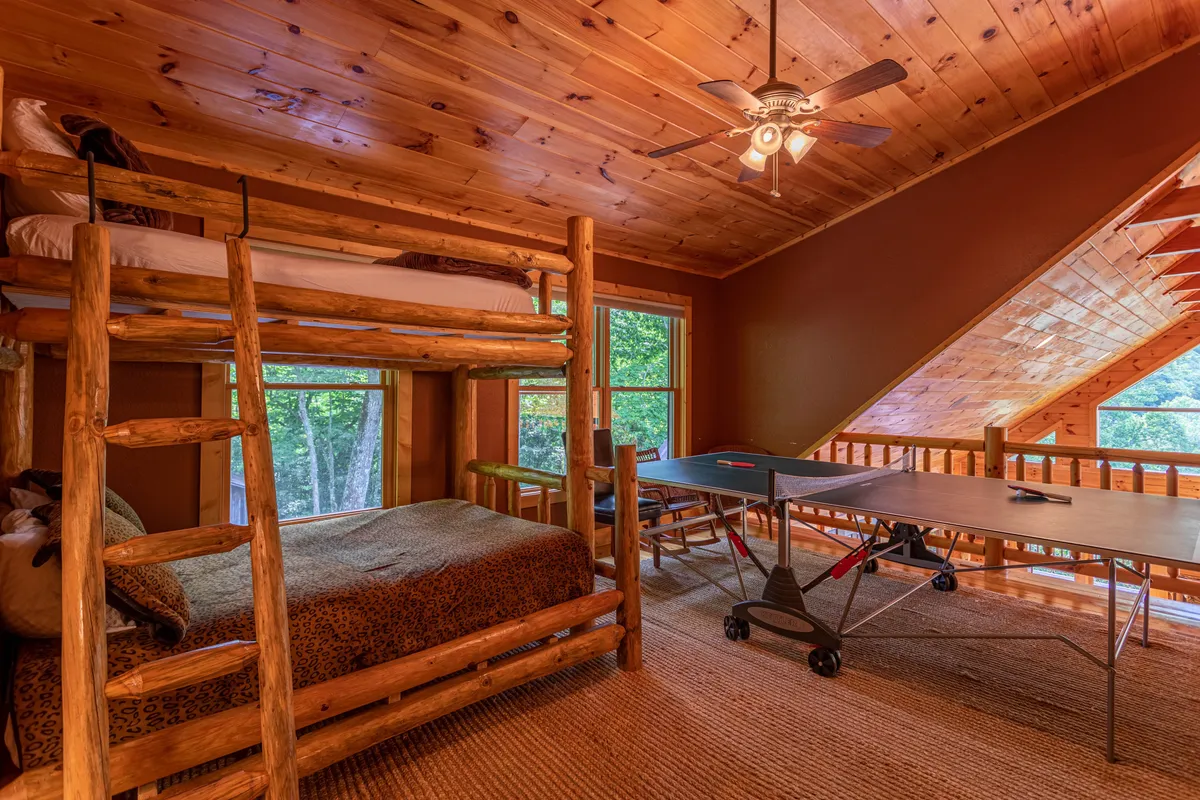 An interior game loft featuring a ping pong table and cozy bunk beds, with large windows letting in plenty of natural light. The space feels playful and inviting, designed for family fun regardless of the weather.