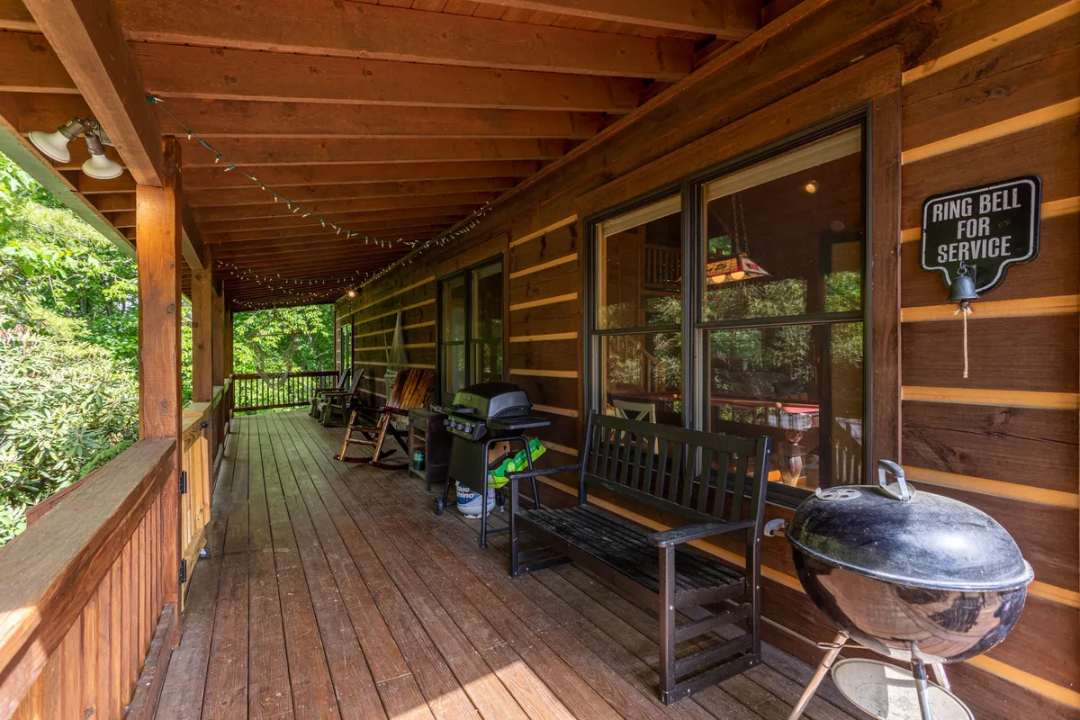 An inviting exterior space with a wooden bench, grill, and rocking chairs under string lights. The setup is perfect for barbecues, storytelling, and group meals, surrounded by nature and a cozy, communal atmosphere.