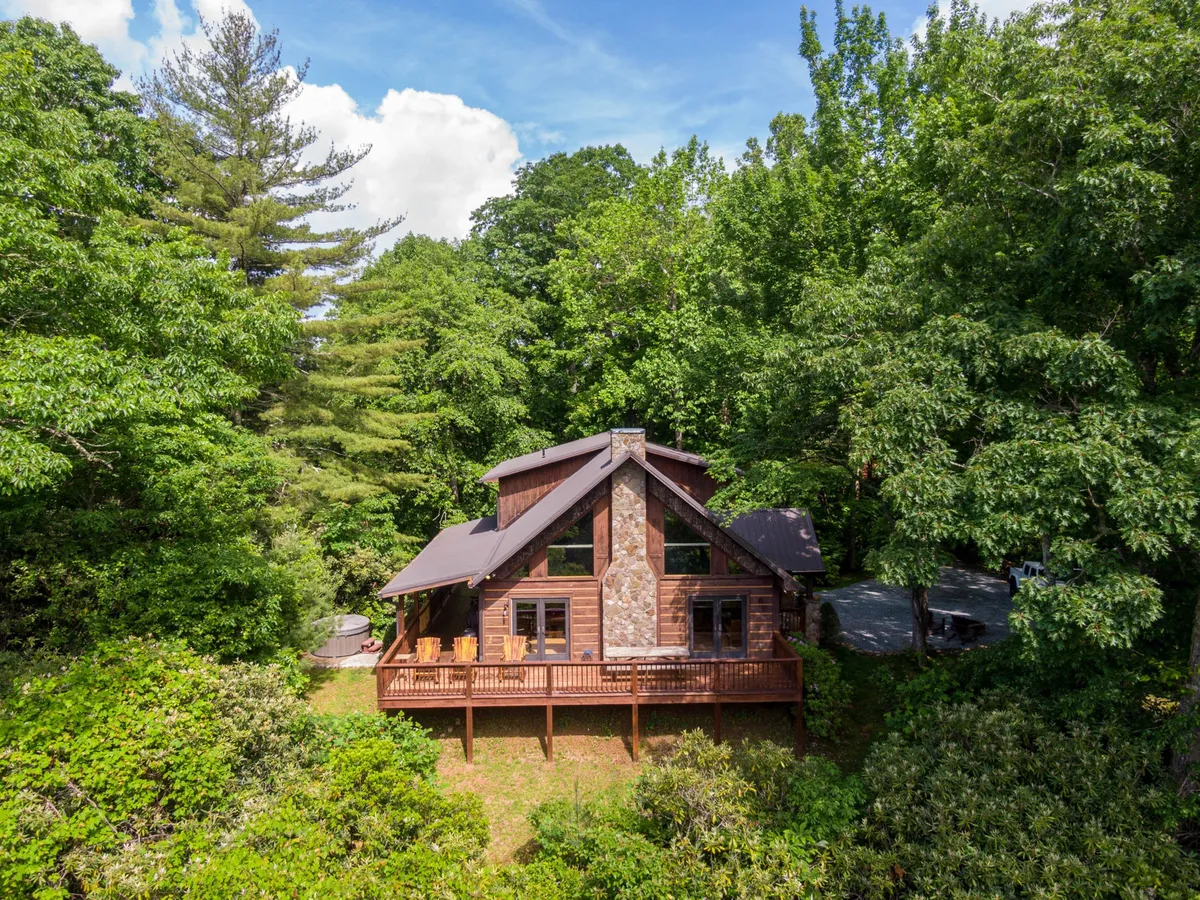 This image depicts a spacious wooden deck with a stone facade, large windows offering expansive views, and lush surrounding trees. The deck is designed for relaxation and gathering, seamlessly connecting the retreat to the outdoors and the natural landscape.