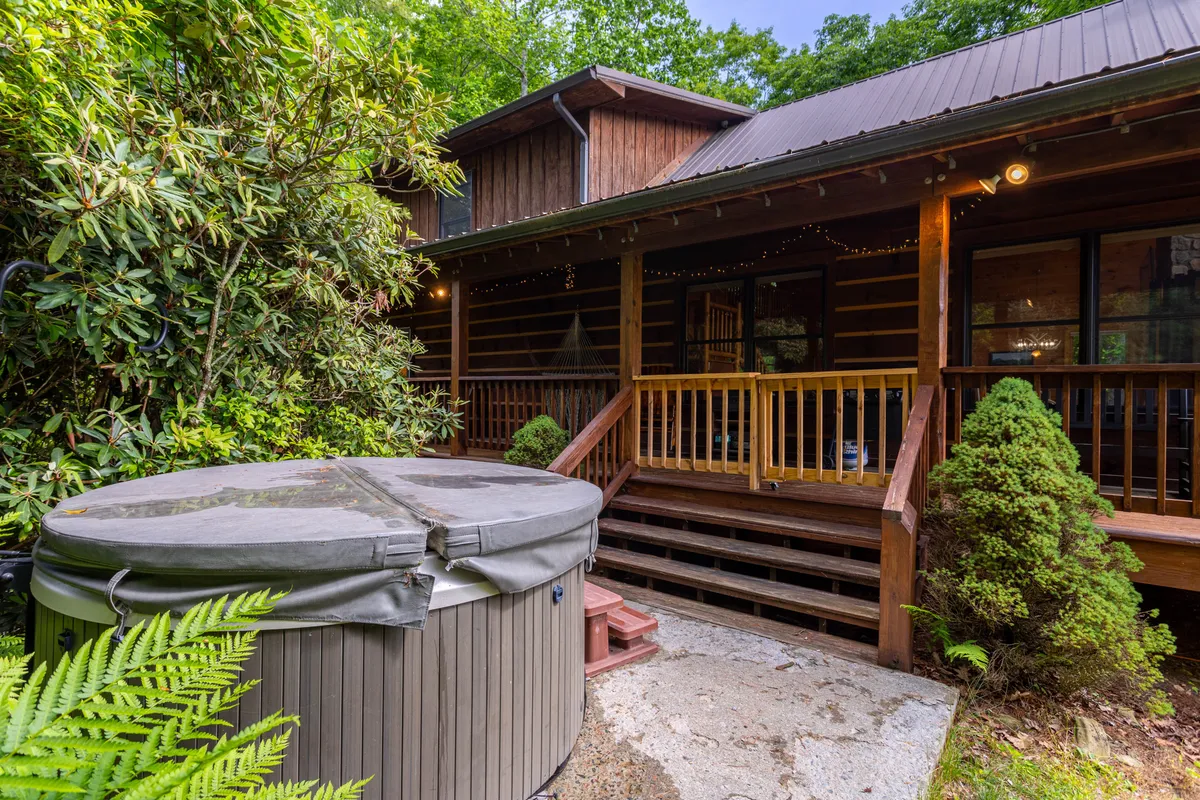 A tranquil scene featuring a hot tub on a wooden deck, surrounded by greenery and situated near the home's entrance. The setting evokes relaxation and offers panoramic views, making it a perfect space for unwinding after a day of mountain adventures.